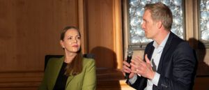 Daniel Terzenbach spricht mit einem Mikrofon auf dem Podium der Nürnberger Gesprächen 2026. Im Hintergrund: Julia Bengerth.