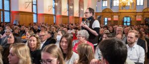 Bei den Nürnberger Gesprächen 2026 stellt ein junger Mann aus dem Publikum im Stehen eine Frage.