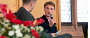Maximilian Hahnenkamp spricht auf dem Podium der Nürnberger Gesprächen 2026 dem Moderator zugewandt in ein Mikrofon.